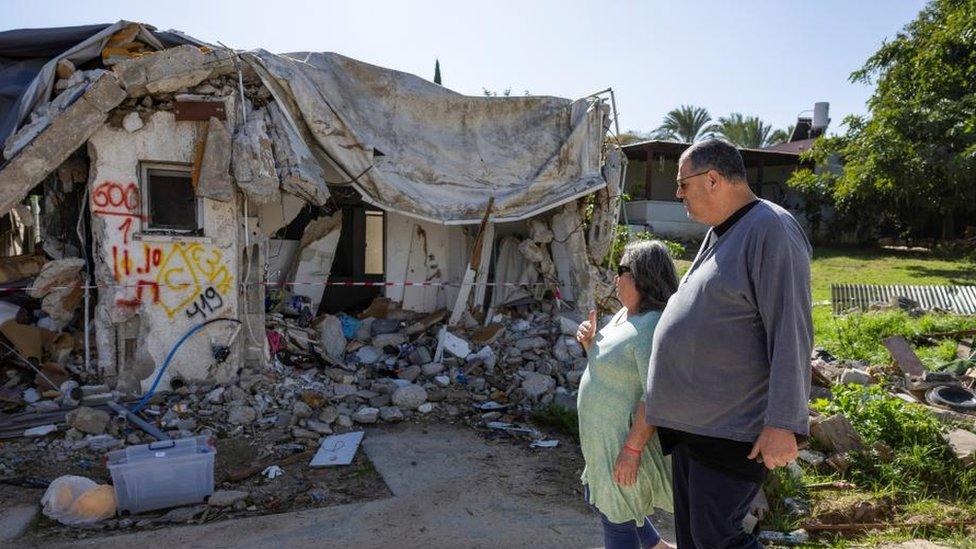 Ayelet Khon and Shachar Shnurman walk past the remains of a home in Kibbutz Kfar Aza in southern Israel, on 13 January 2024