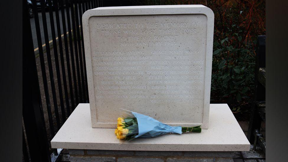 A memorial stone with yellow roses placed beside it