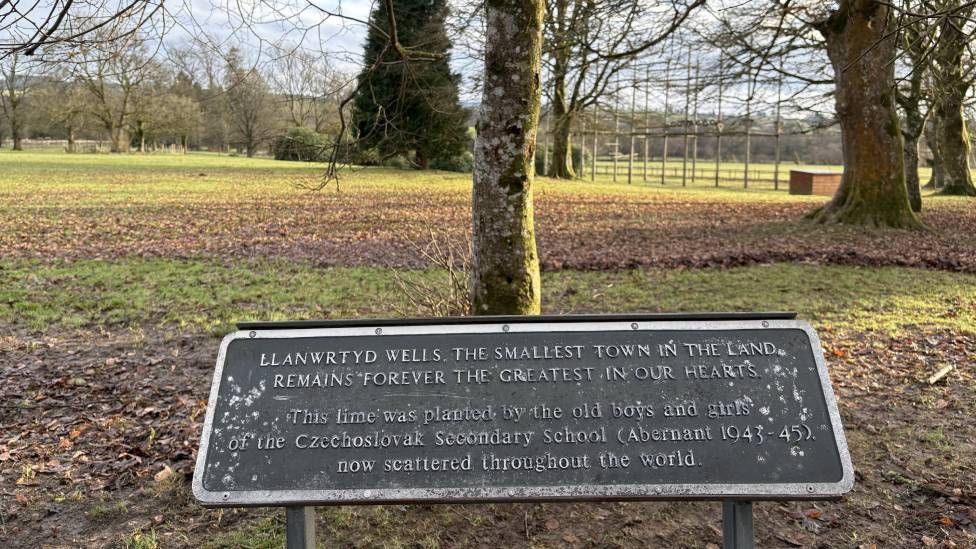 A plaque that reads Llanwrtyd Wells, the smallest town in the land, remains the greatest in our heart beneath a tree 