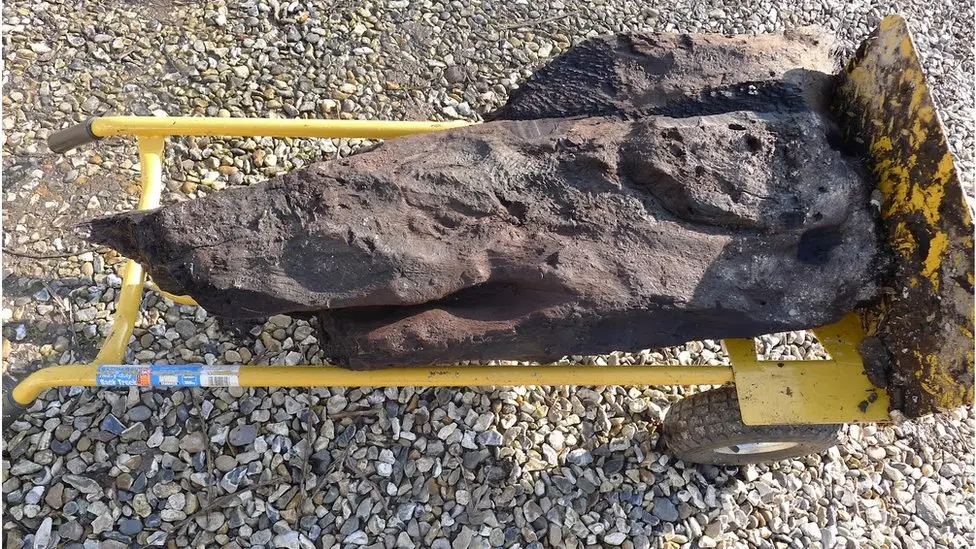 The carved piece of wood on a yellow trolley on a stony driveway.