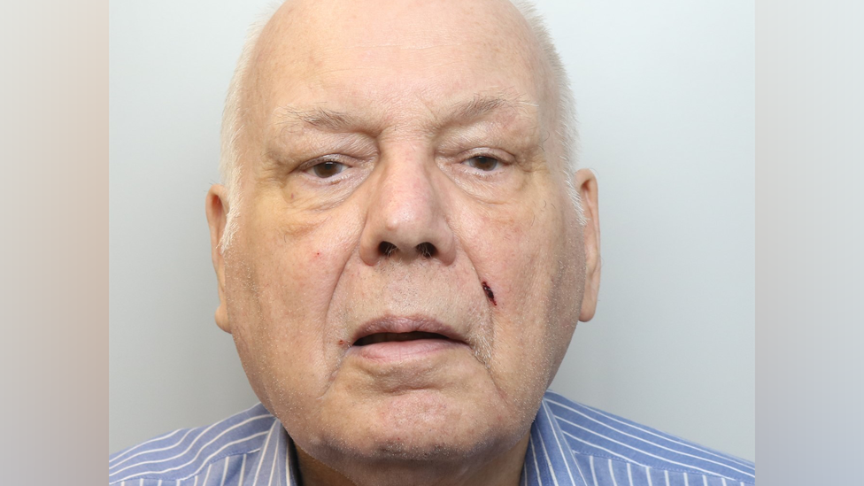 A 2024 police mugshot, showing Burrows as an older man, with thin white hair and wearing a blue stripped shirt