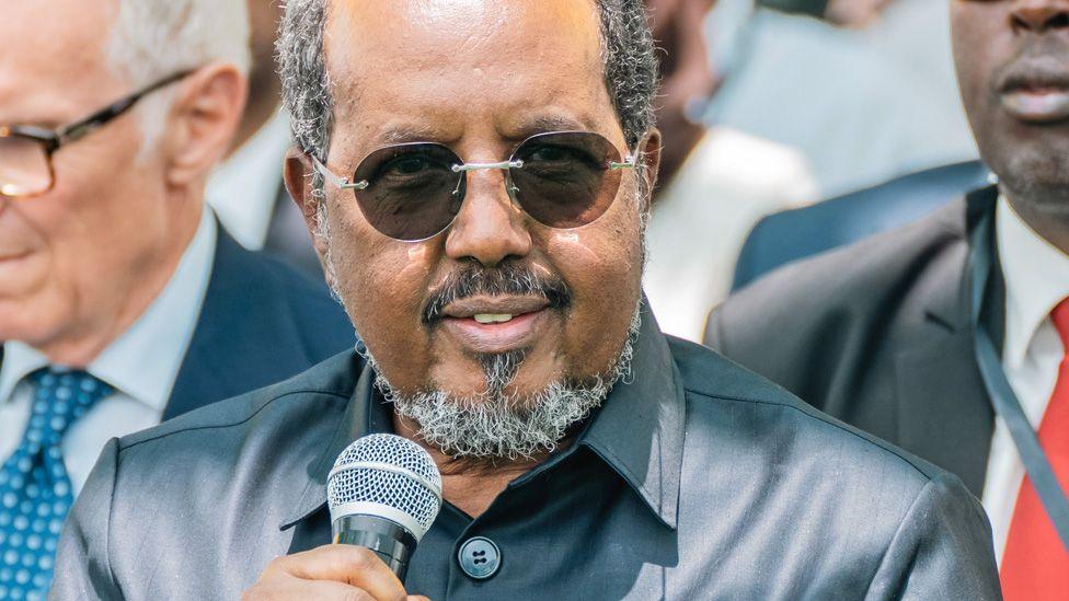 Hassan Sheikh Mohamud, Somalia's president, wearing sunglasses and dressed in buttoned jacket, holds a microphone.
