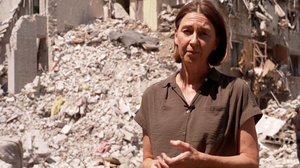 Sarah Rainsford qısaqollu qəhvəyi köynəkdə, Kiyevdə dağıntıların qarşısında