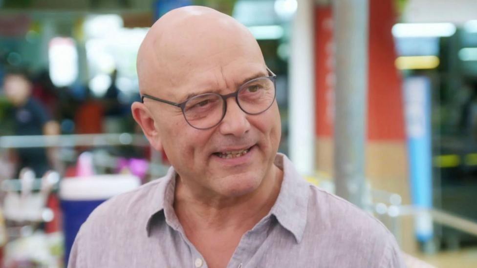 A picture of Gregg Wallace wearing a light coloured shirt against a colourful background