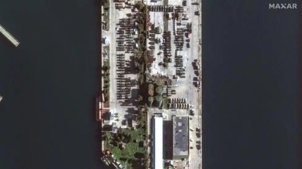 Military vehicles at Tartous port on 17 December. They are parked in rows with greenery buildings surrounding them. 

