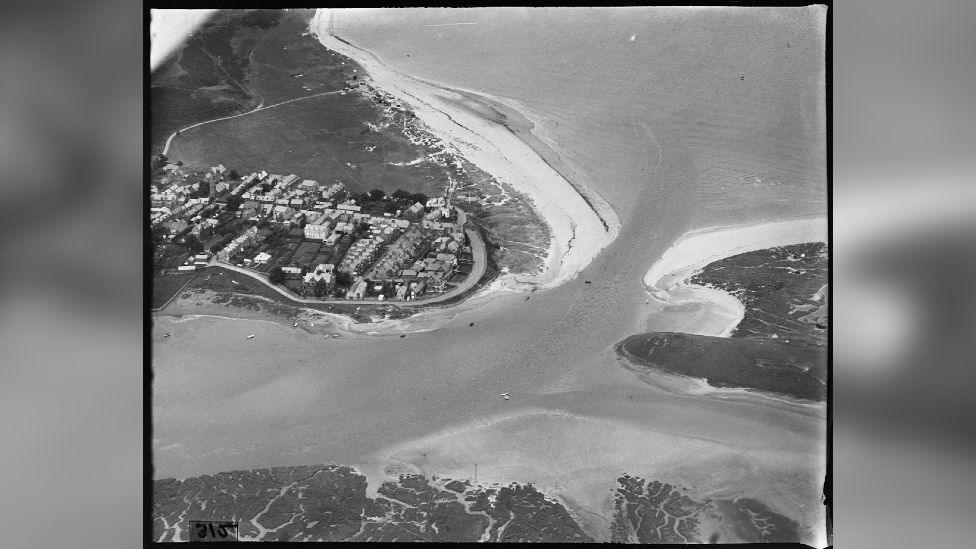 A black-and-white aerial shot of two coastlines meeting at the sea.