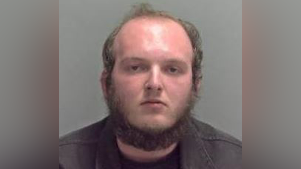 Connor Yaxley appears in his police custody photo, with a beard, receding hairline and dark coloured jacket. 