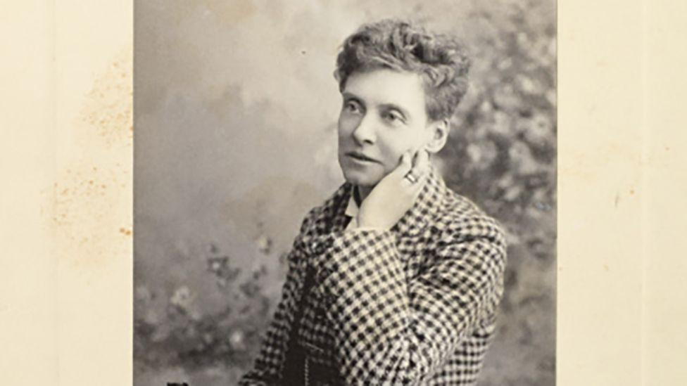 Black and white photograph of Emily Langton Massingberd she has short hair and is wearing a black and white checked jacket