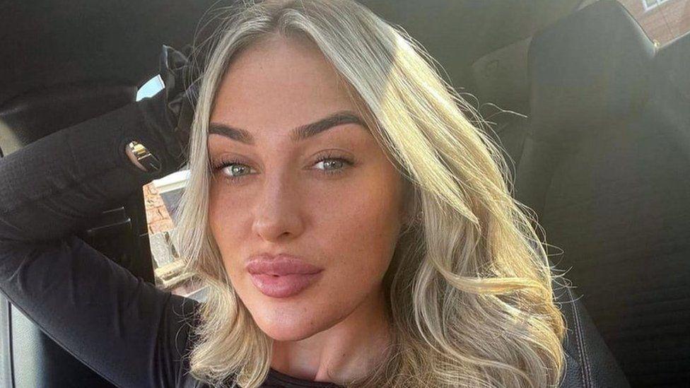 Elle Edwards, who has blonde hair, poses for a selfie in the seat of a car with her right hand behind her head