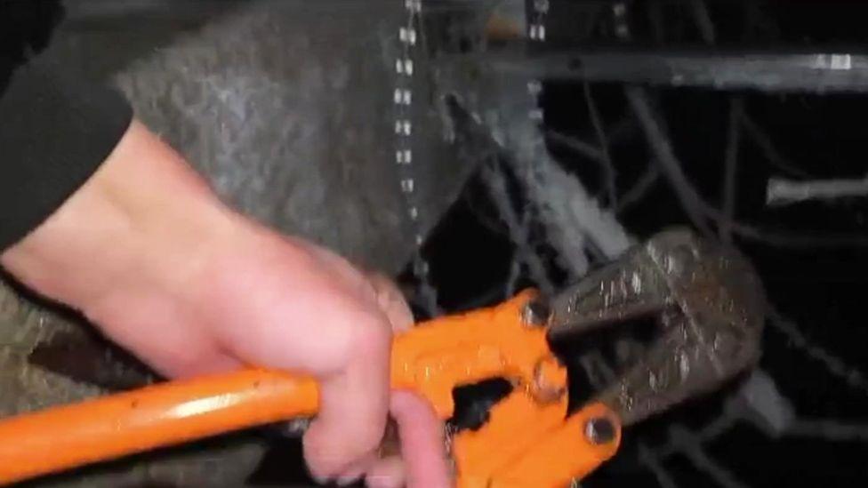 Hands operate orange wirecutters in the dark