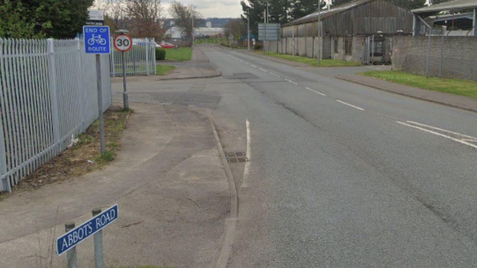 A general view of Abbots Road with buildings on one side and metal fencing on the other