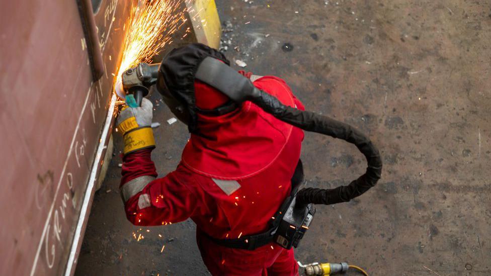 Person in high tech protective gear using a blowtorch at the Harland & Wolff shipyard in Belfast