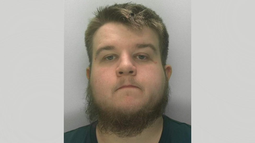 A police mugshot of Taran Jay Woodward. He is has a brown-coloured beard and is wearing a dark green top.