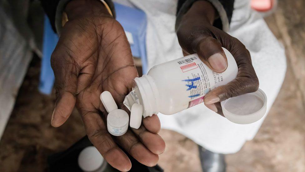 A close up of a woman's hand as she pours ARV tablets on to her palm from a white container.