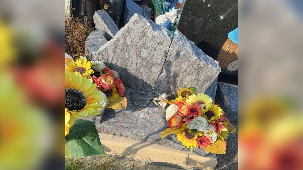 A broken gravestone with flowers on it.