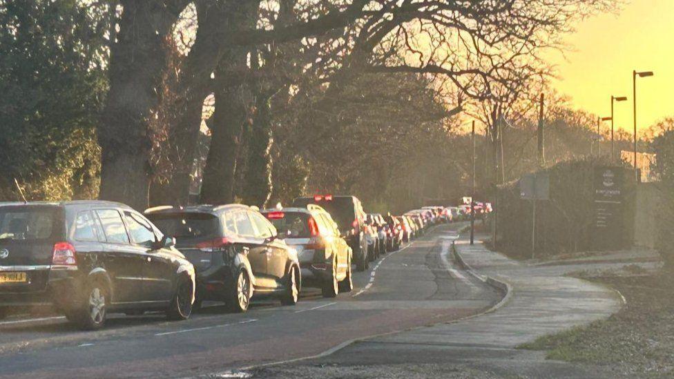 Queue of cars on left of road snaking away into the distance.