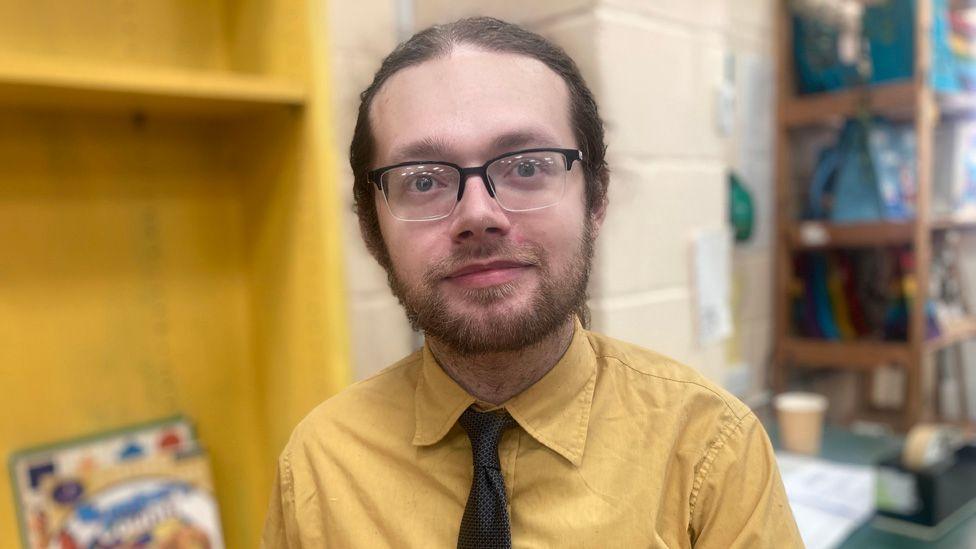 Henrik Burton in a yellow shirt and black tie standing next to book called numbers counta book 