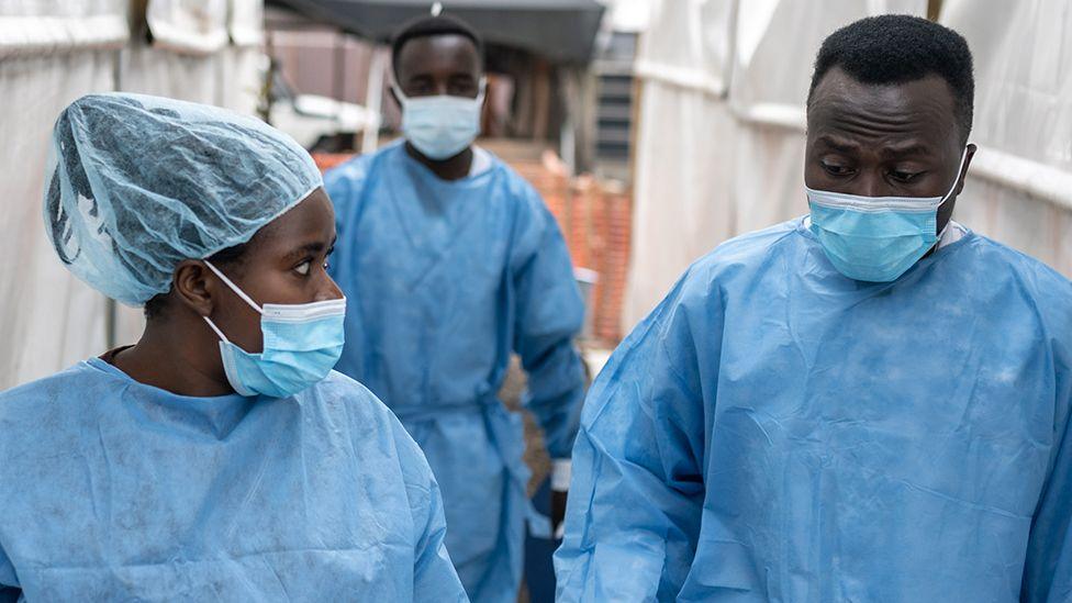 Health workers wearing masks and scrubs chat as they walk in between tents at the Munigi mpox treatment centre in North Kivu, DR Congo on 17 August