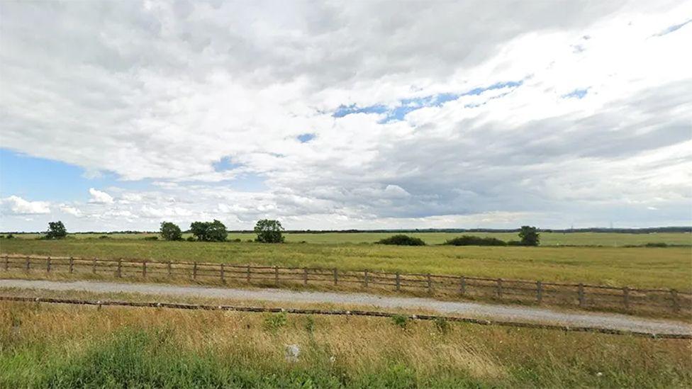 A Google Streetview picture of the current site with trees in an open field