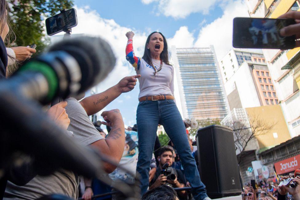 Venezuelan opposition leader Maria Corina Machado addressing a protest rally, with her arm raised in the air as she speaks