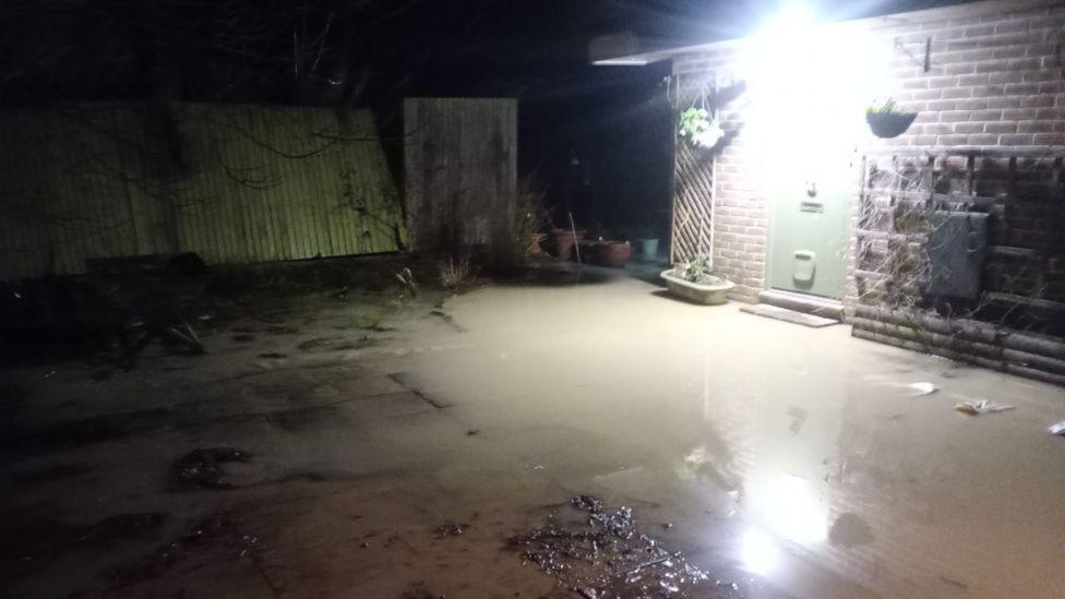 Sewer water outside the a property. There is a light on above a door and a fence to the left. 