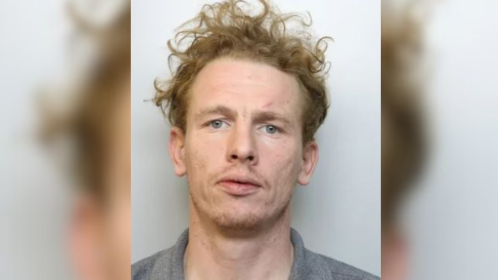 A police custody photo of Jeremiah Connors. He has curly hair and is wearing a grey jumper.