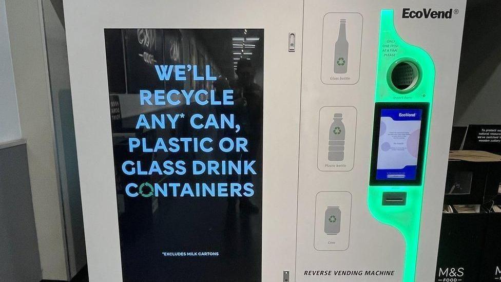 Image of a "reverse vending machine" apparently in an M&S Food store featuring a large screen which says "we'll recycle any can, plastic or glass drink containers"