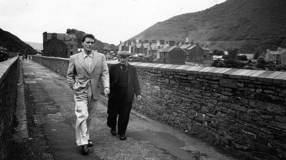 A black and white image of Richard Burton and his father Richard Jenkins Senior crossing a bridge in their home town of Pontrhydyfen, during one of Burton's visits home after he became famous.