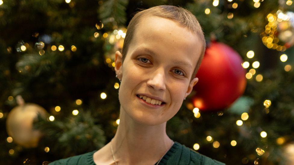 A headshot of Liz Hatton smiling and looking at the camera, against a backdrop of a christmas tree with baubles