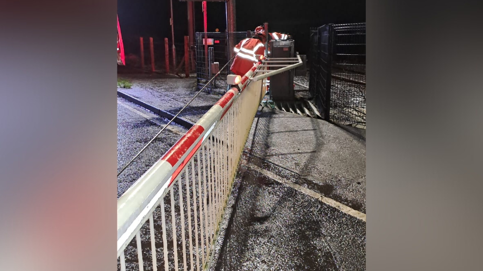 A worker in an orange high visibility jacket works at a railway crossing