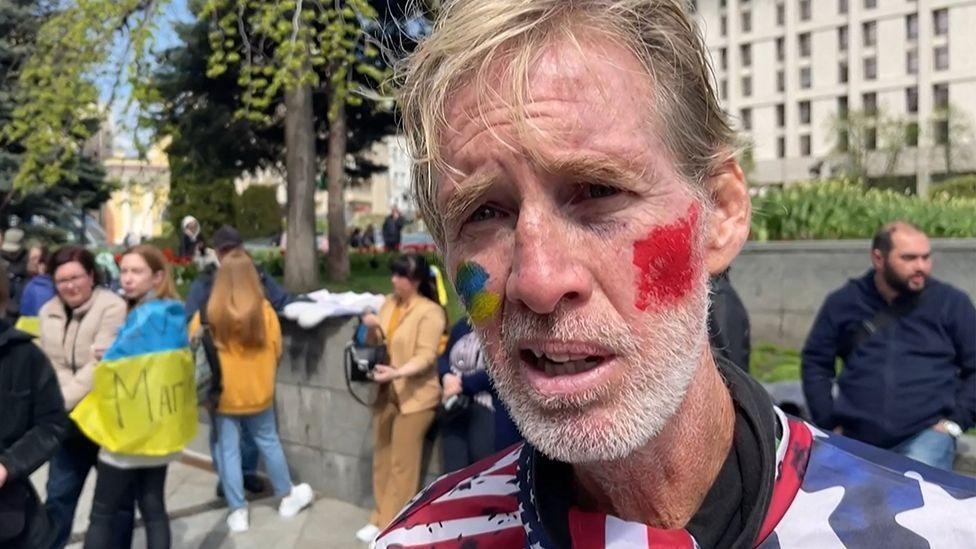 Screengrab from APTV on 16 September shows Ryan Routh head and shoulders shot as he is interviewed by AFP with colours of the US flag painted on his cheeks, with other campaigners and a Ukraine flag in the backround, in Kyiv on 27 April 2022