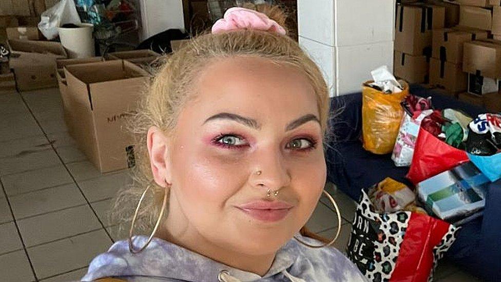 A woman takes a selfie in front of bags of clothes