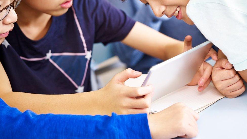 Stock image of three boys using a tablet in class