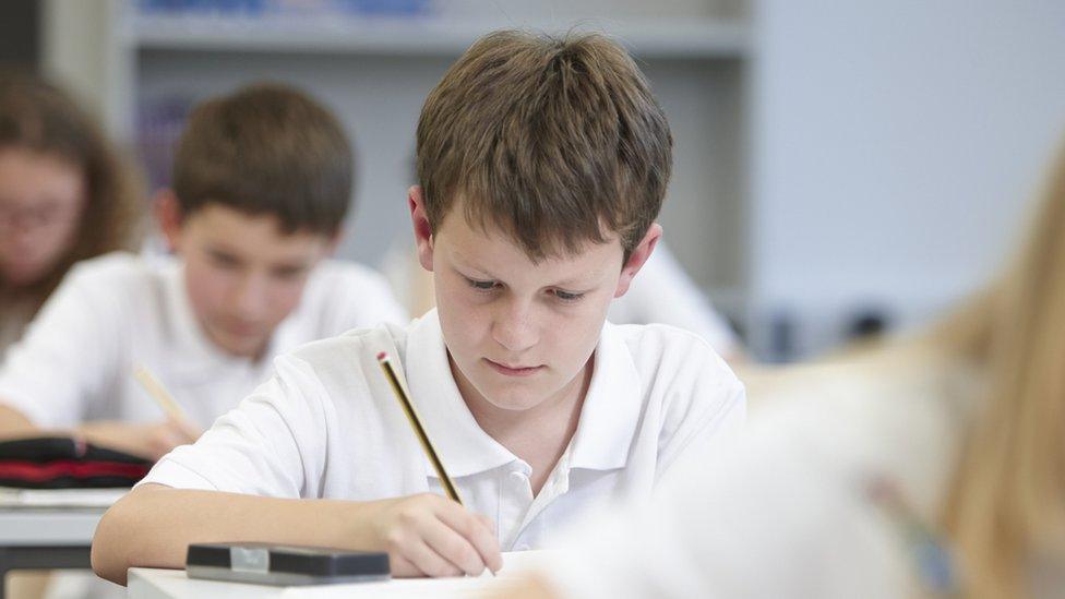 A group of young people doing a test in an exam setting. The child in focus is a young male with brown hair