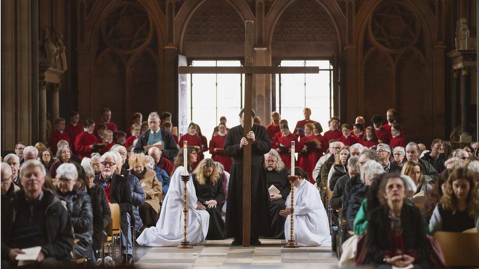 Worshippers sit in their seats on Good Friday at Bristol Cathedral as a wooden cross is brought in