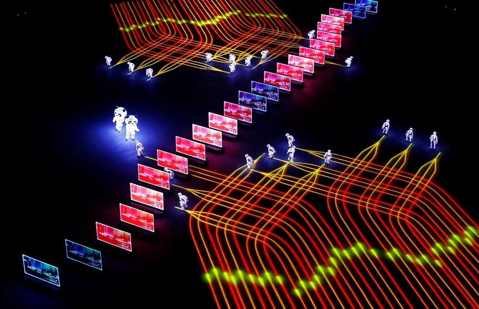 Artists perform as yellow and red lines of light follow behind them