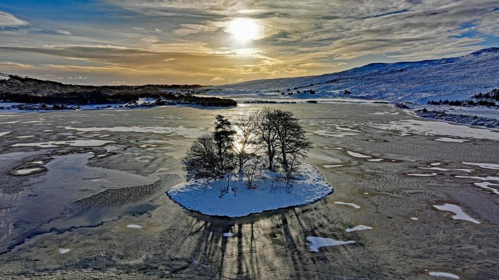 A frozen lake with small snow-covered islands and the sun shining overhead