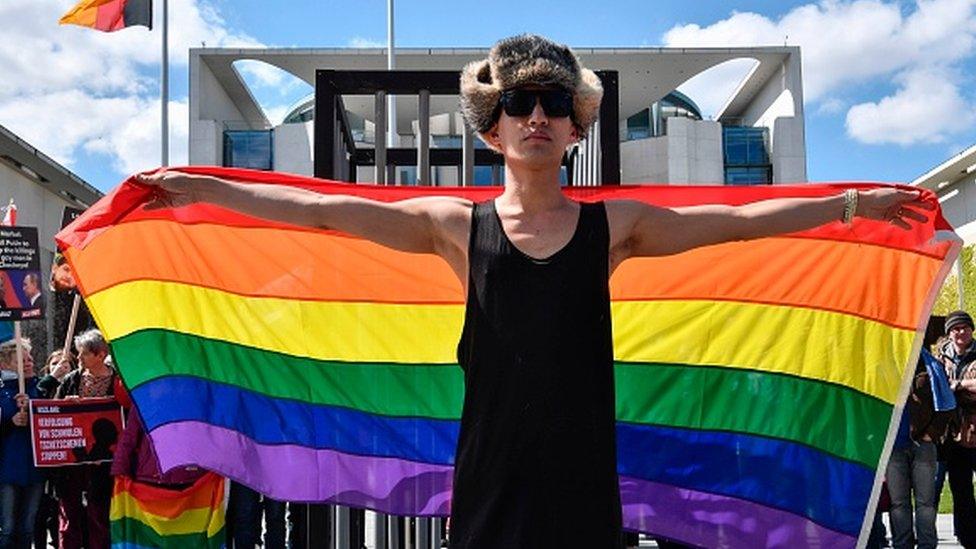 An activist displays a rainbow flag in front of the Chancellery in Berlin during a demonstration calling on the Russian president to put an end to the persecution of gay men in Chechnya (30 April 2017)