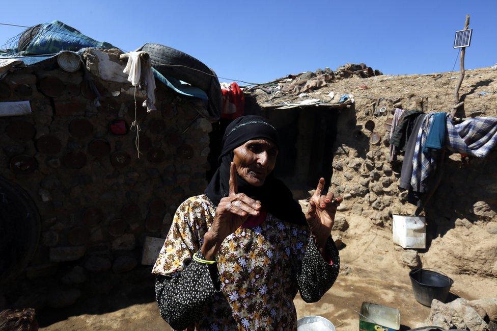 An elderly woman gestures to the camera