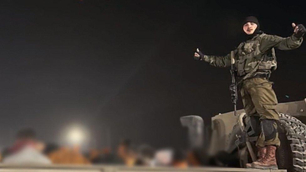 An IDF soldier stands on a pickup truck with blindfolded detainees