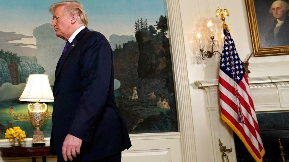 Donald Trump walks out of frame, left, off-centre, with the White House decor and US flag in the background