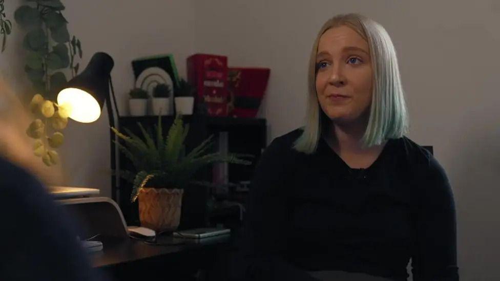 Stefanie Harman sat by her desk in her home talking to the BBC. She grey-white hair in a bob and is wearing a black top.