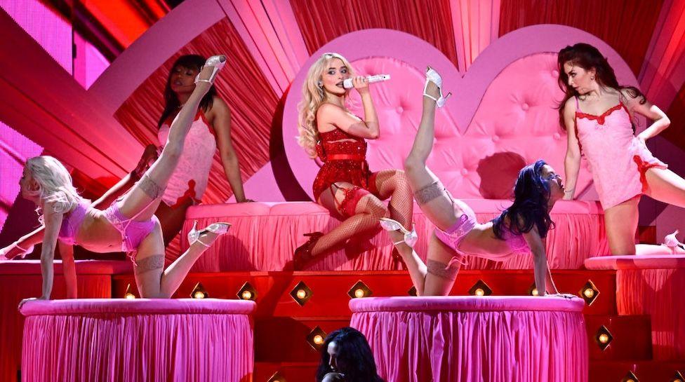 Sabrina Carpenter in a red outfit surrounded by dancers in pink