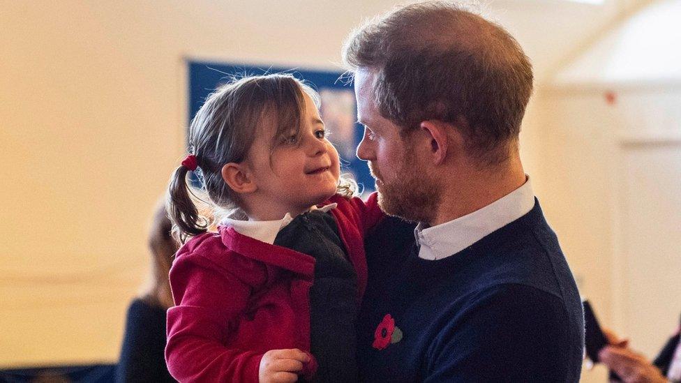 Prince Harry picks up a little girl at Windsor's Broom Farm Community Centre