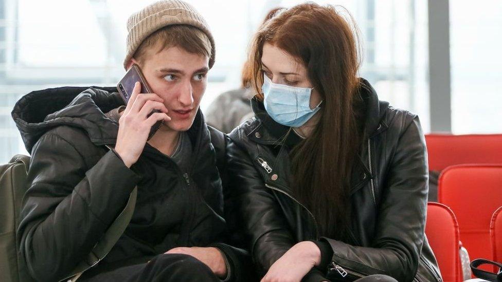 A young woman wearing a face mask looks at her unmasked partner at a train station in the Russian city of Sochi