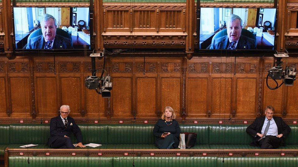 MPs sit in the chamber listening to a colleague on Zoom