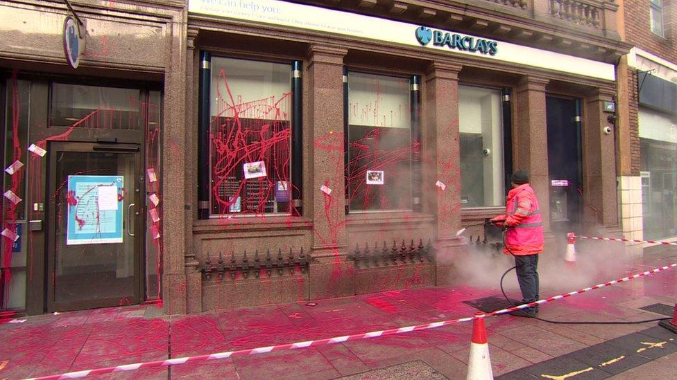 A man cleaning red paint from a Barclays branch