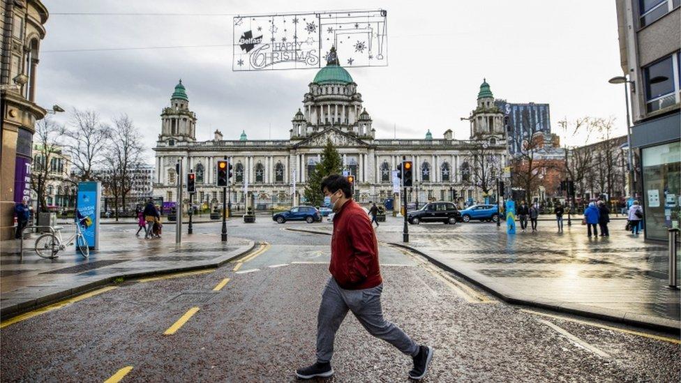 A man wearing a mask walks along Donegall Place in front of Belfast City Hall