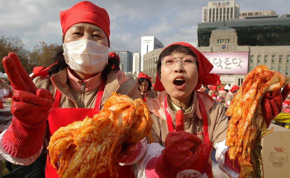 Two ladies holding up kimchi at a public kimchi-making event in Seoul