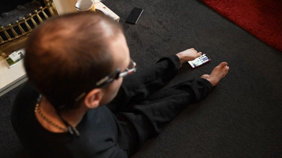 A man scrolling through a phone with his toes